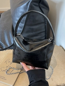 Glossy black pleated handbag with silver chain strap shown in a lifestyle setting