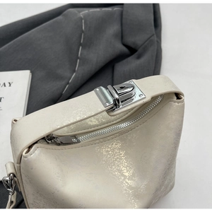 Detail of the pearlescent off-white bucket bag with silver metal lock and textured finish