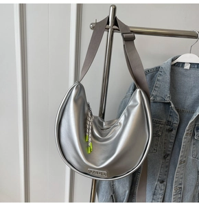 Détail du sac croissant argenté avec bandoulière large et plaque logo VADU en métal