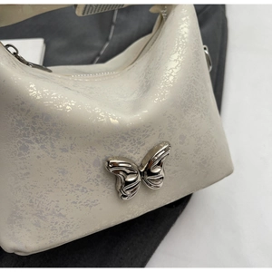 Close-up of silver butterfly metallic clasp and textured cream white faux leather bag