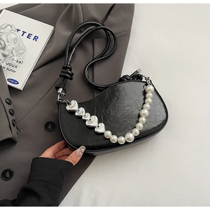 Detailed shot of crescent bag featuring pearly heart chain and crinkled leather texture