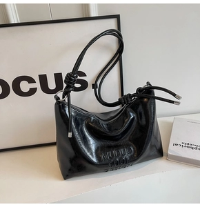Detail of glossy black underarm bag featuring knotted shoulder strap and embossed logo