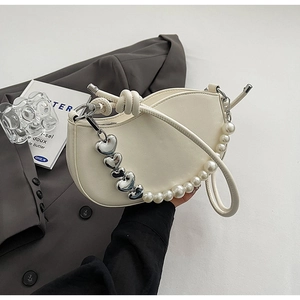 Detailed close-up of cream crescent bag with decorative pearl and heart strap