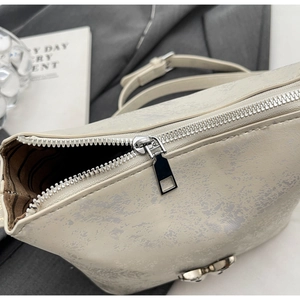 Detail of cream bucket bag with distressed texture, silver butterfly buckle, and zipper