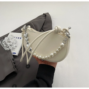 Detailed shot of cream half-moon bag with pearl chain and silver heart pendant