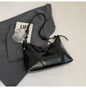 Detail of black glossy shoulder bag with MUDUO COOL DESIGN embossing and knotted strap
