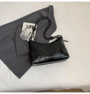 Detail of the glossy black faux leather shoulder bag with a unique knotted strap design