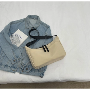 Detail of minimalist beige dumpling bag with adjustable strap and textured nylon surface