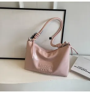 Detail of pink glossy shoulder bag featuring knot handle design and embossed lettering