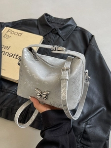 Silver bucket bag with butterfly metal accent on black leather background