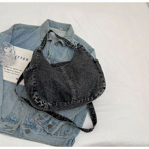 Détail macro du denim noir délavé vintage et des poches latérales sur le sac à bandoulière
