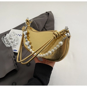Detailed shot of golden crescent bag featuring pearl chain and heart-shaped metal charms