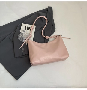 Detail of light pink crescent underarm bag on a suit, featuring decorative strap knots