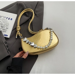 Detailed view of golden metallic underarm bag with pearl and heart chain decoration