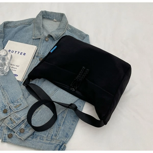 Detail of black dumpling bag with wide adjustable strap and blue label on white fabric