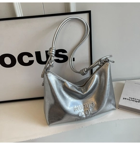 Detail of silver metallic underarm bag with embossed text and knotted shoulder strap