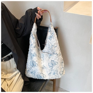 Detail showing plush cream tote bag with blue butterfly embroidery and brown leather strap