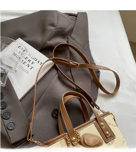 Detail of adjustable brown leather shoulder strap and gold chain on cream bucket bag
