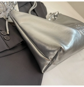 Close-up of metallic silver tote bag featuring embossed logo texture and knotted strap detail