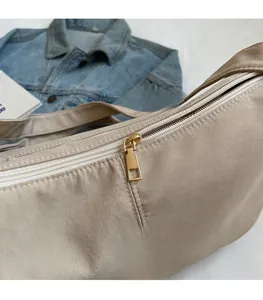 Detail of smooth gold zipper and ifashion patch on beige pleated crescent bag