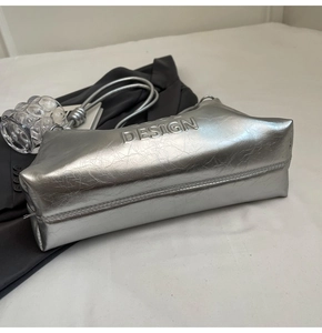 Detail of silver metallic rectangle shoulder bag with crinkled texture and DESIGN lettering