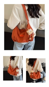 Detail view of large brick red canvas tote bag with adjustable strap and plush pendant