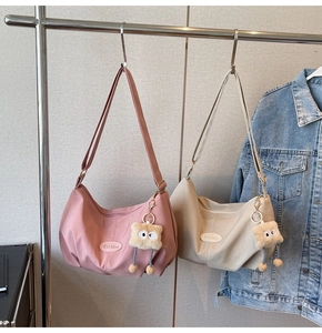 Pink and khaki crescent tote bags with plush pendants shown in a lifestyle display
