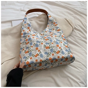 Detail showing the floral canvas embroidery and brown leather handle of the tote bag