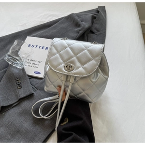 Gros plan détaillé d'un mini sac à dos argenté matelassé sur tissu gris avec accessoires