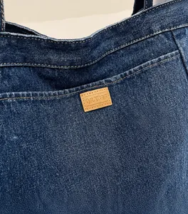 Details von dunkelblauem Denim-Tote-Stoff mit Doppelnaht und braunem Lederetikett
