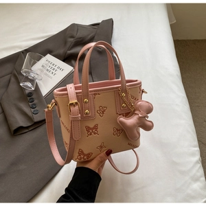 Detail view of beige leather tote with butterfly pattern and pink gingerbread charm