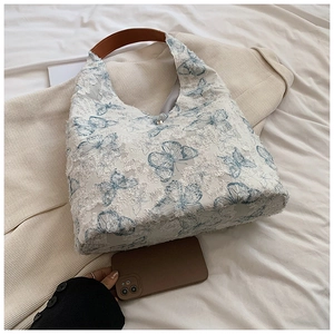 Detail of blue lace butterfly embroidery on off-white tote bag with brown leather strap