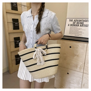Detailed close-up of woven straw tote bag with black stripes and white lace bow