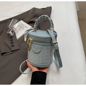Detail of light blue woven bucket bag with scarf-wrapped handle and gold chain charm