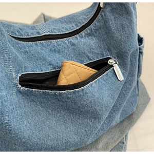 Détail d'un sac bandoulière en jean avec poche zippée latérale et ferrures métalliques