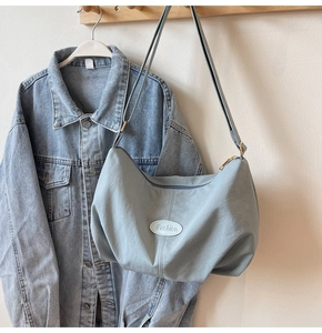 Detail of light blue crescent nylon bag with adjustable strap on a minimalist wooden rack