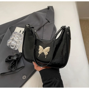 Dettaglio borsa a mezzaluna nera con texture screpolata lucida e rilievo a farfalla bianca