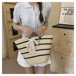 Detail of a woven straw tote bag with black stripes and a cream lace bow accessory