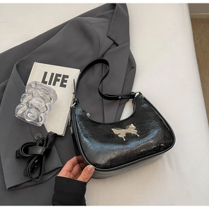 Dettaglio borsa hobo in pelle nera increspata con ciondolo a fiocco d'argento e tracolla