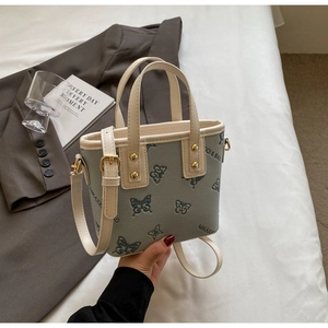Detail of gray-green bucket bag with butterfly relief and cream-colored handle texture