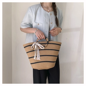 Detail of hand-woven straw tote bag with black stripes and white lace bow decoration