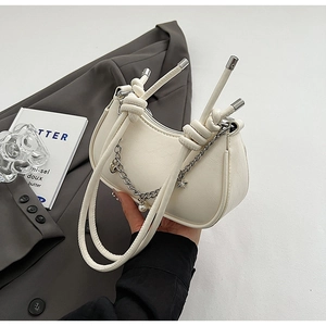Detail of cream white crescent bag featuring silver chain charms and knotted handle design