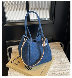 Detailed view of dark blue denim bucket bag featuring light brown leather accent and brand tag