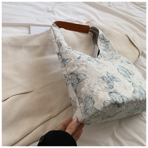 Detailed shot of white canvas tote with 3D blue butterfly embroidery and brown leather strap