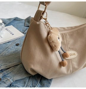 Detail of beige crescent crossbody bag with fashion patch and cute plush charm accessory