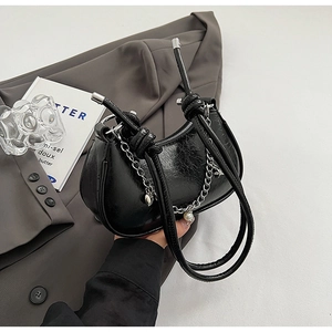 Detail of black wrinkled patent leather shoulder bag with silver chain and pearl charms