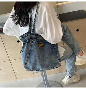 Detailansicht der hellblauen Jeans-Tragetasche mit seitlichem Kordelzug und Logo-Aufnäher aus Leder