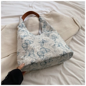 Detailed shot of white lace tote bag featuring blue butterfly embroidery and leather handles