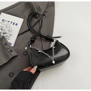 Detail of black glossy half-moon bag with silver chain and pearl on a grey suit background