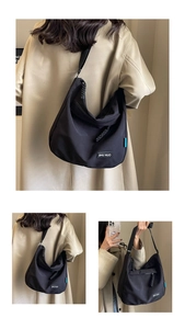 Detail of minimalist black nylon messenger bag featuring woven zipper and shoulder strap
